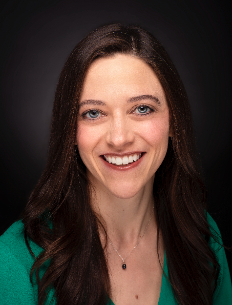 A woman with long brown hair and a green top, smiling with a dark gradient background.              